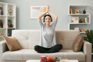 Joven mujer realizando yoga en la sala de su hogar para aminorar el estres
