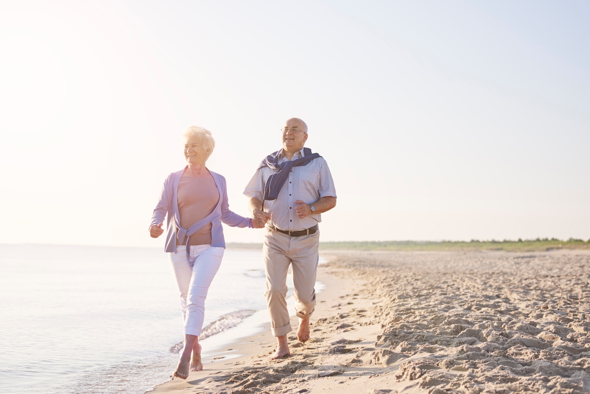 Pareja de la tercera edad trotandop por la orilla de la playa disfrutando de su tiempo