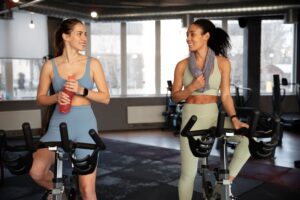 Par de amigas realizando bicicleta en el gimnasio del desarrollo inmobiliario donde viven