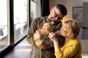 Pareja adulto mayores haciéndole cariños y mimos a su mascota gato con pelaje dorado