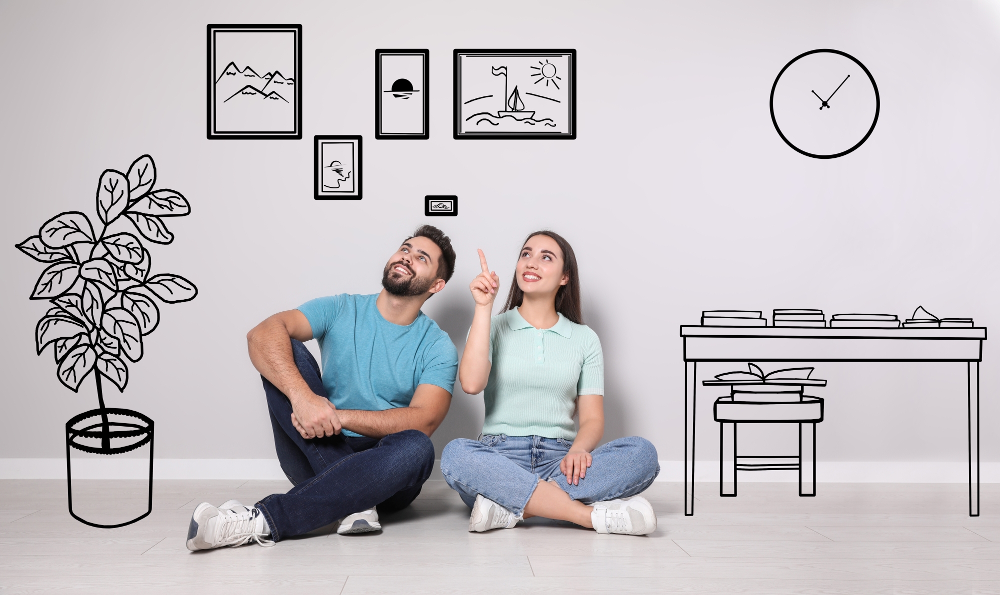 Pareja feliz sentada en el piso recargados a la pared planeando el acomodo de la decoración en la pared se visualiza a través de dibujos cómo quedan colocados los cuadros, reloj de pared, planta y un pequeño escritorio