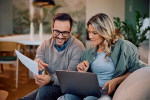 Pareja sonriente revisando las finanzas de su hogar en casa