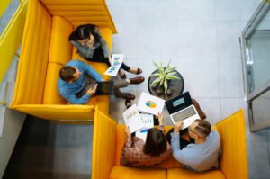 Área de coworking amenidad de desarrollo inmobiliario jovenes emprendedores presentando proyectos sentados en muebles color amarillo
