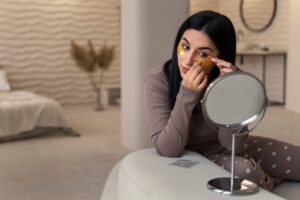 Mujer disfrutando de su rutina de belleza con parches dorados para los ojos utilizando espejos pequeños en la habitación