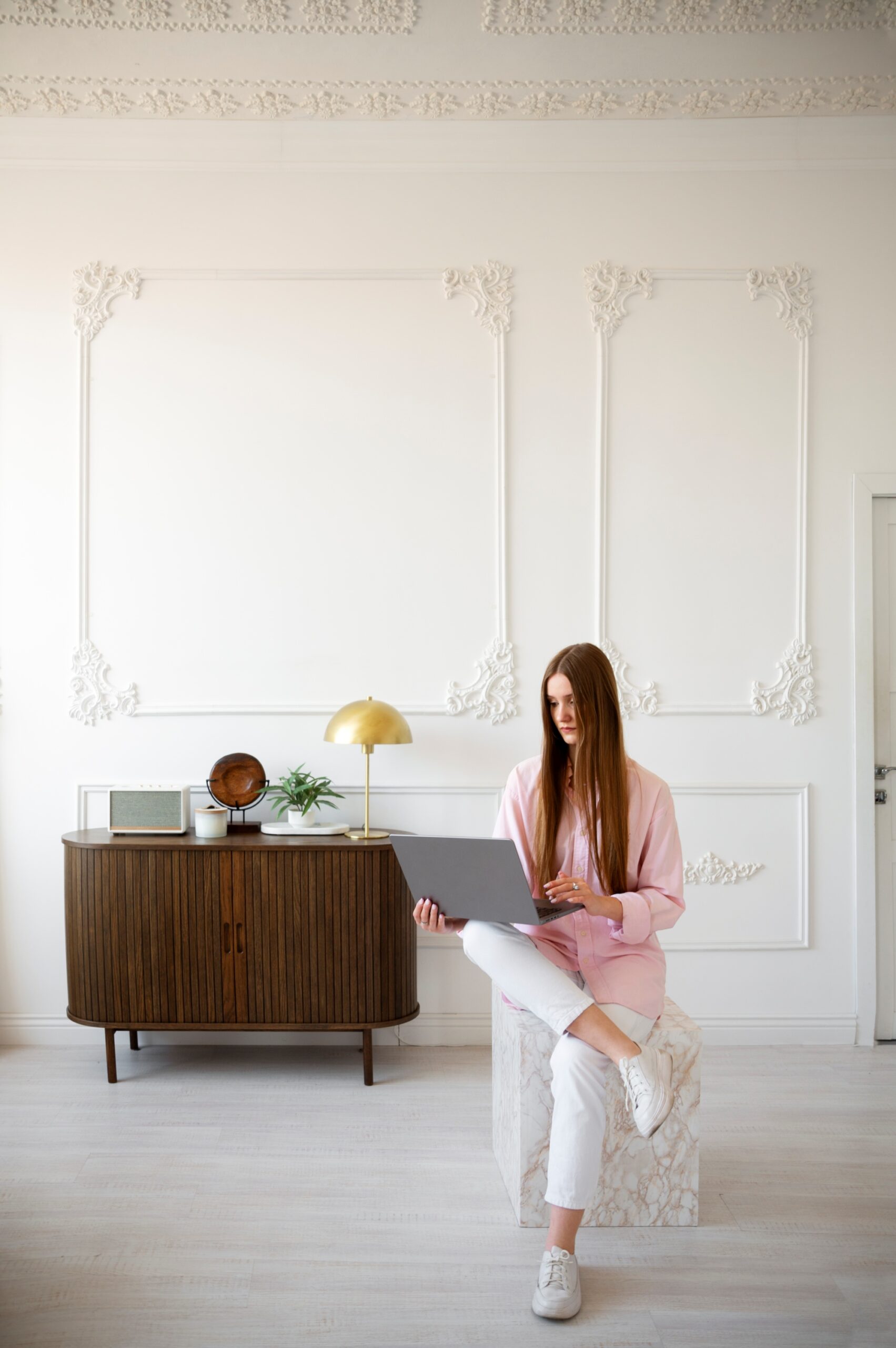 Mujer usando computadora portátil en habitación decorada minimalista con detalles en pared con molduras blancas genera amplitud, iluminación confort tranquilidad