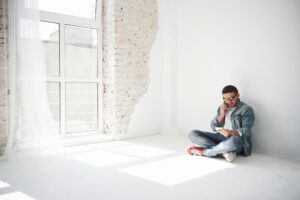 joven sentado en el piso hablando por teléfono en un espacio en color con textura en ladrillo en blanco hace que resalte el ambiente dando un toque sofisticado