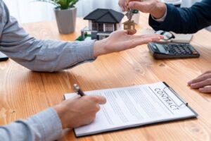 Agente inmobiliario entregando la llave de la casa arrendada y arrendatario firmando el contrato