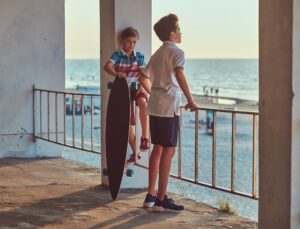 dos-hermanos-pequenos-parados-con-una-patineta-cerca-de-la-barandilla-contra-el-fondo-de-la-costa-al-atardecer