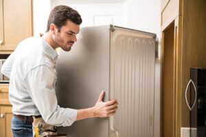 Detalles del adjunto joven-que-trabaja-como-electricista-exponiendo-la-parte-trasera-de-una-nevera-para-revisarla-y-repararla